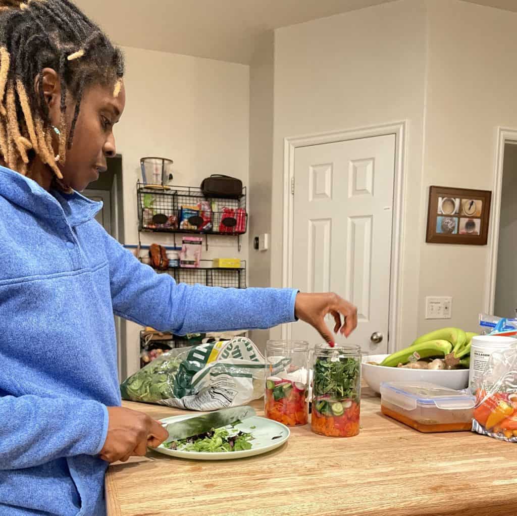 Malika in a blue hoodie preparing a salad