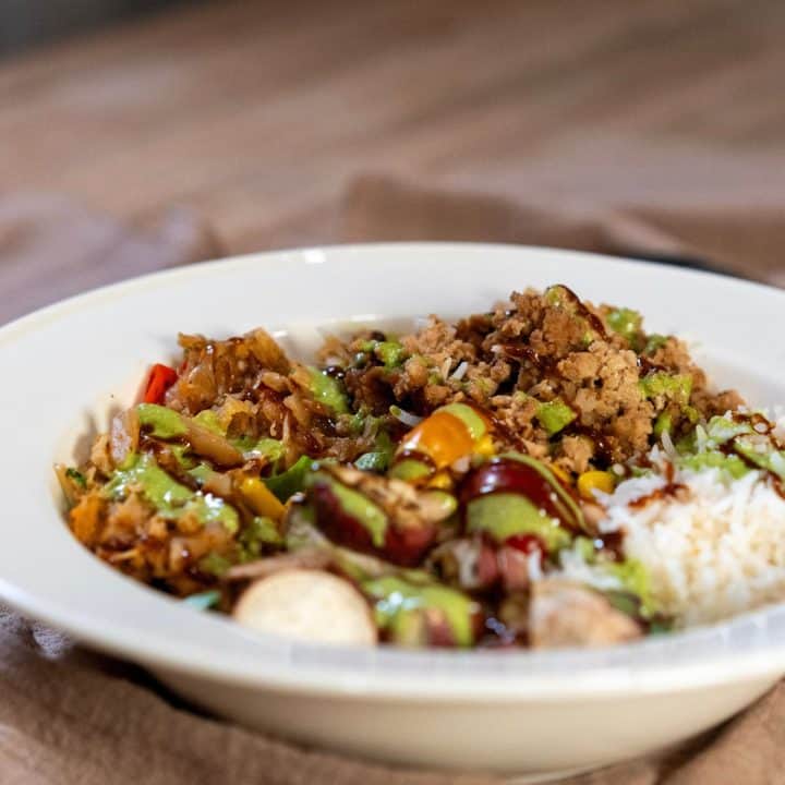 Plate of yummy teriyaki tofu with rice, beans, sauté onions, greens and red peppers, Japanese sweet potatoes, tomatoes with a tasty parley-mint lime dressing
