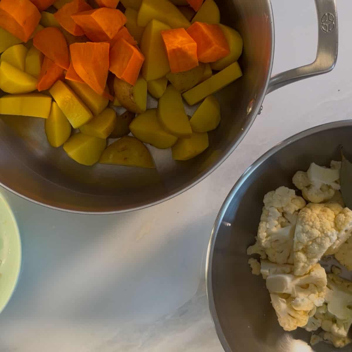 2 pots on a table, one filled with the normal and sweet potatoes cubes and the other one with cubes of cauliflower