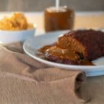 a plate of mushroom vegan meatloaf with some vegan gravy and a side of mashed potatoes in the back