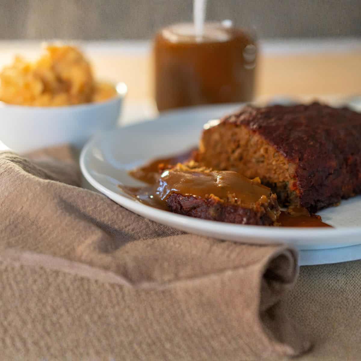 a plate of mushroom vegan meatloaf with some vegan gravy and a side of mashed potatoes in the back