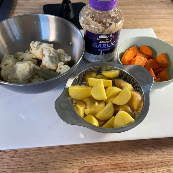 showing of the ingredients needed to make the low calorie mashed potatoes: normal and sweet potatoes, cauliflower and garlic