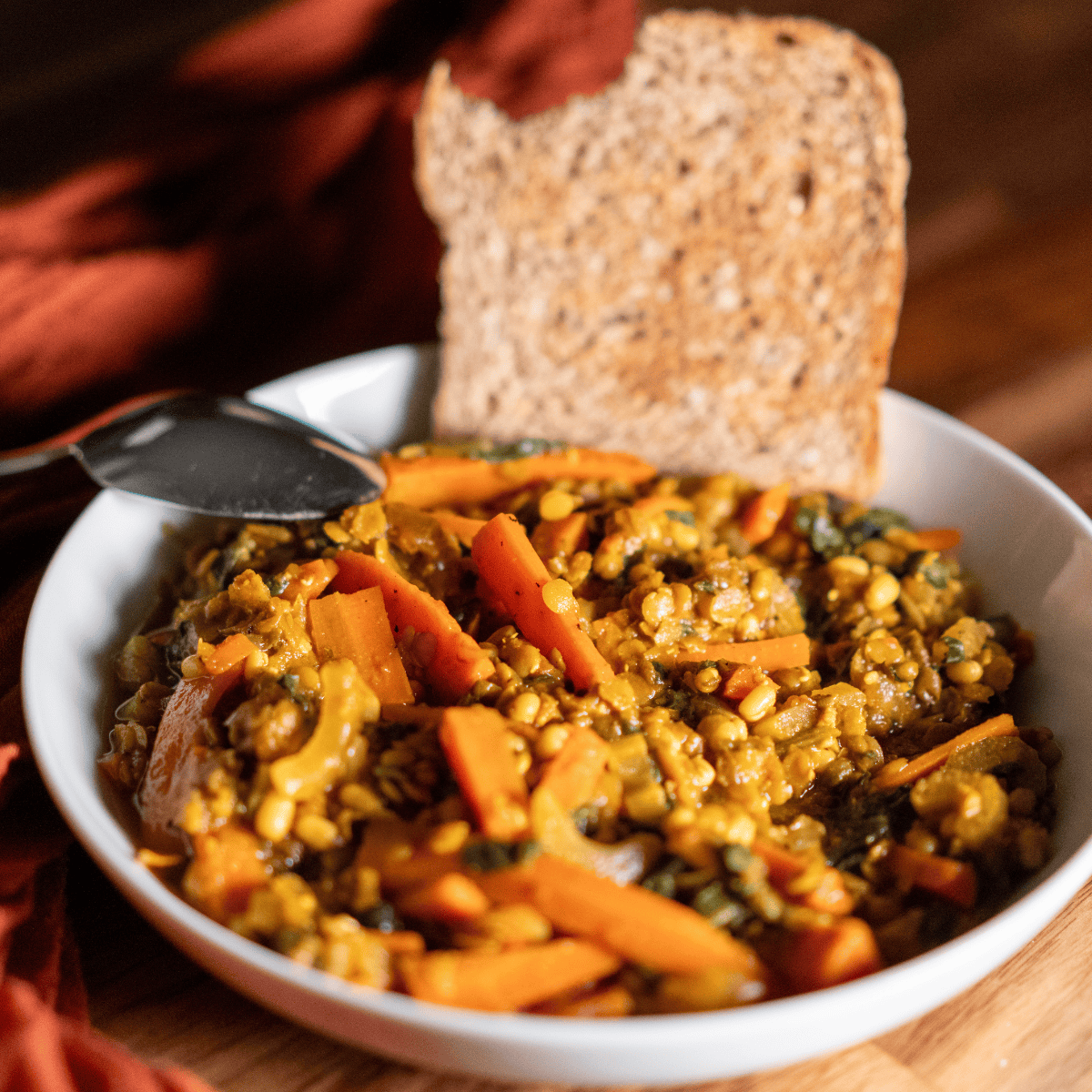 Savory lentil vegetable stew with carrots and spices served with whole grain bread in a white bowl.