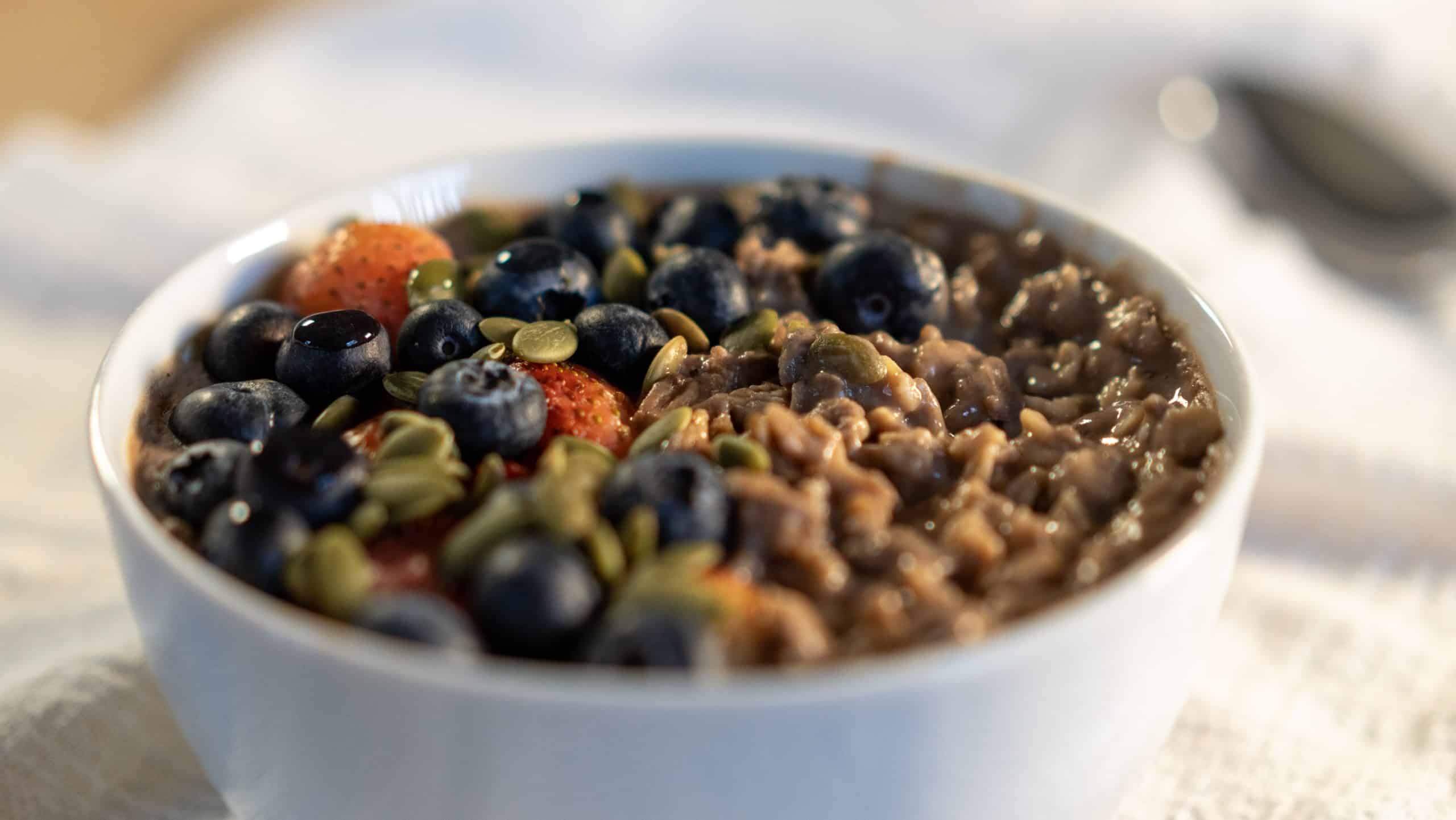 chocolate oatmeal with protein serve in a bowl tap with fresh blueberries, strawberries and pumpkin seeds