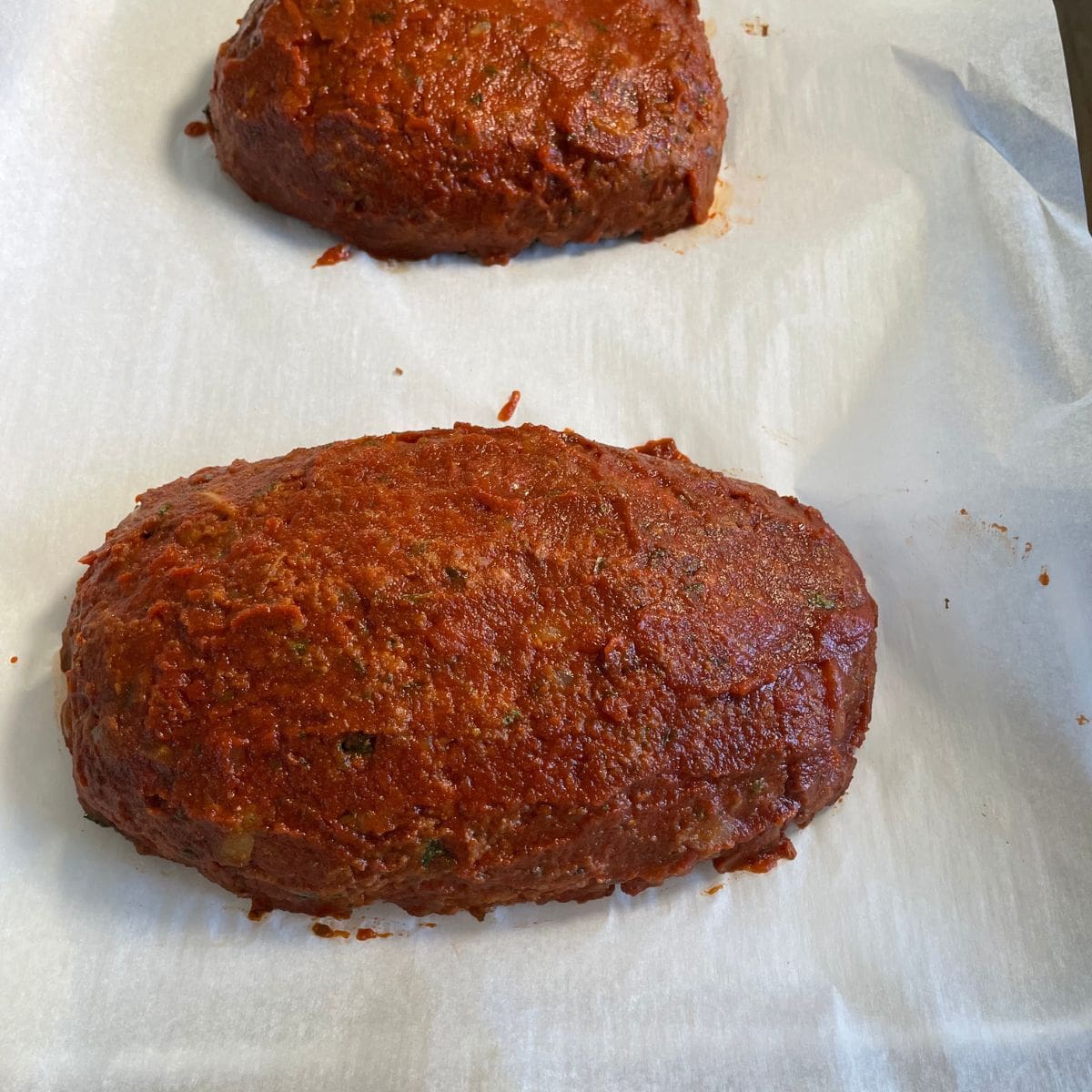 vegan meatloaf shaped put in a pan top with the tomato topping and ready to be baked