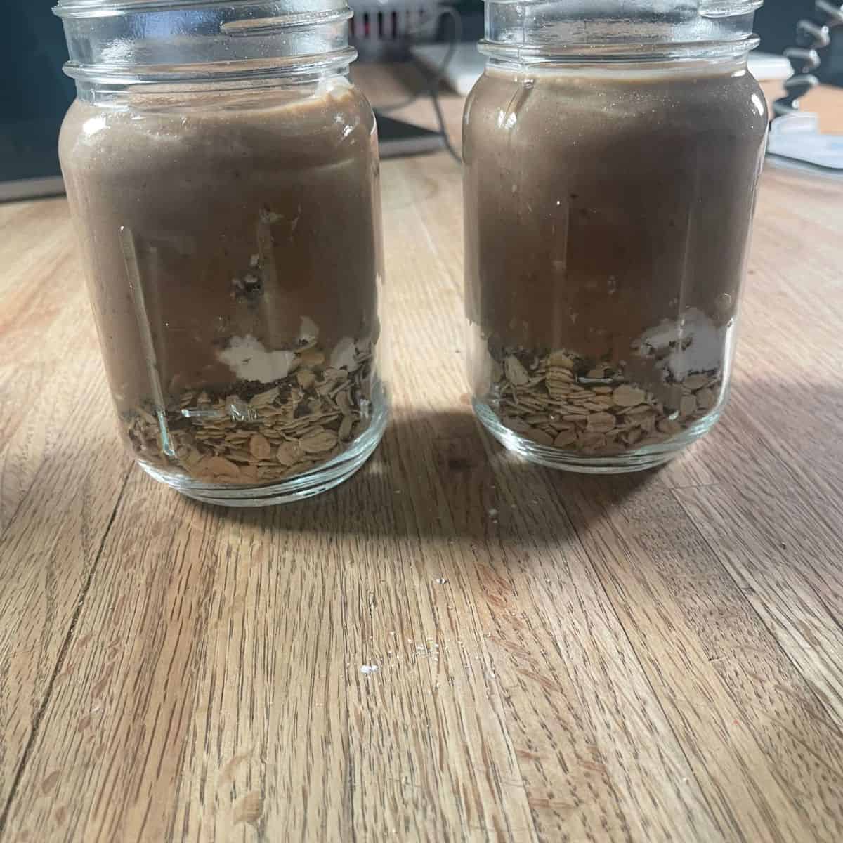 two glass jars showing the oats, chia, creatine and creamy base ready to be combined