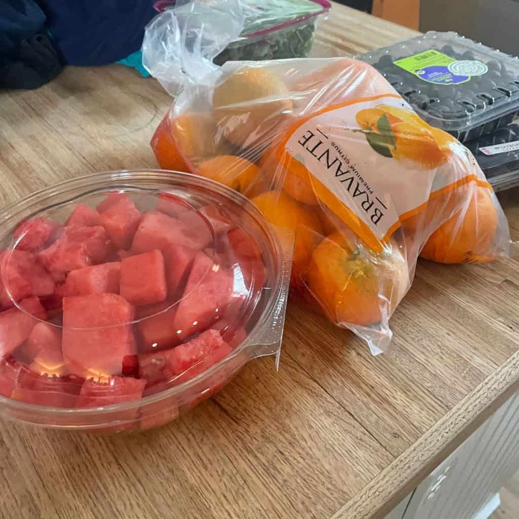Fresh watermelon cubes in a clear plastic container on a wooden table.