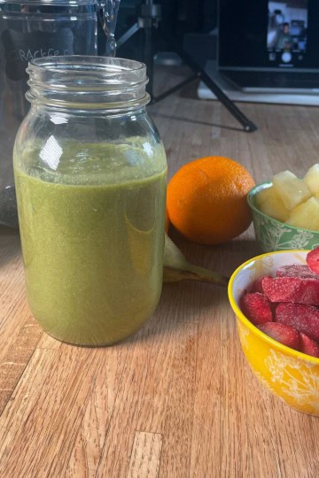 Fresh green smoothie with pineapple, strawberries, and orange on a wooden table.