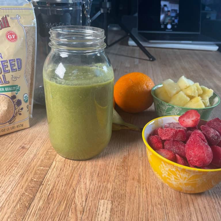 Fresh green smoothie with pineapple, strawberries, and orange on a wooden table.