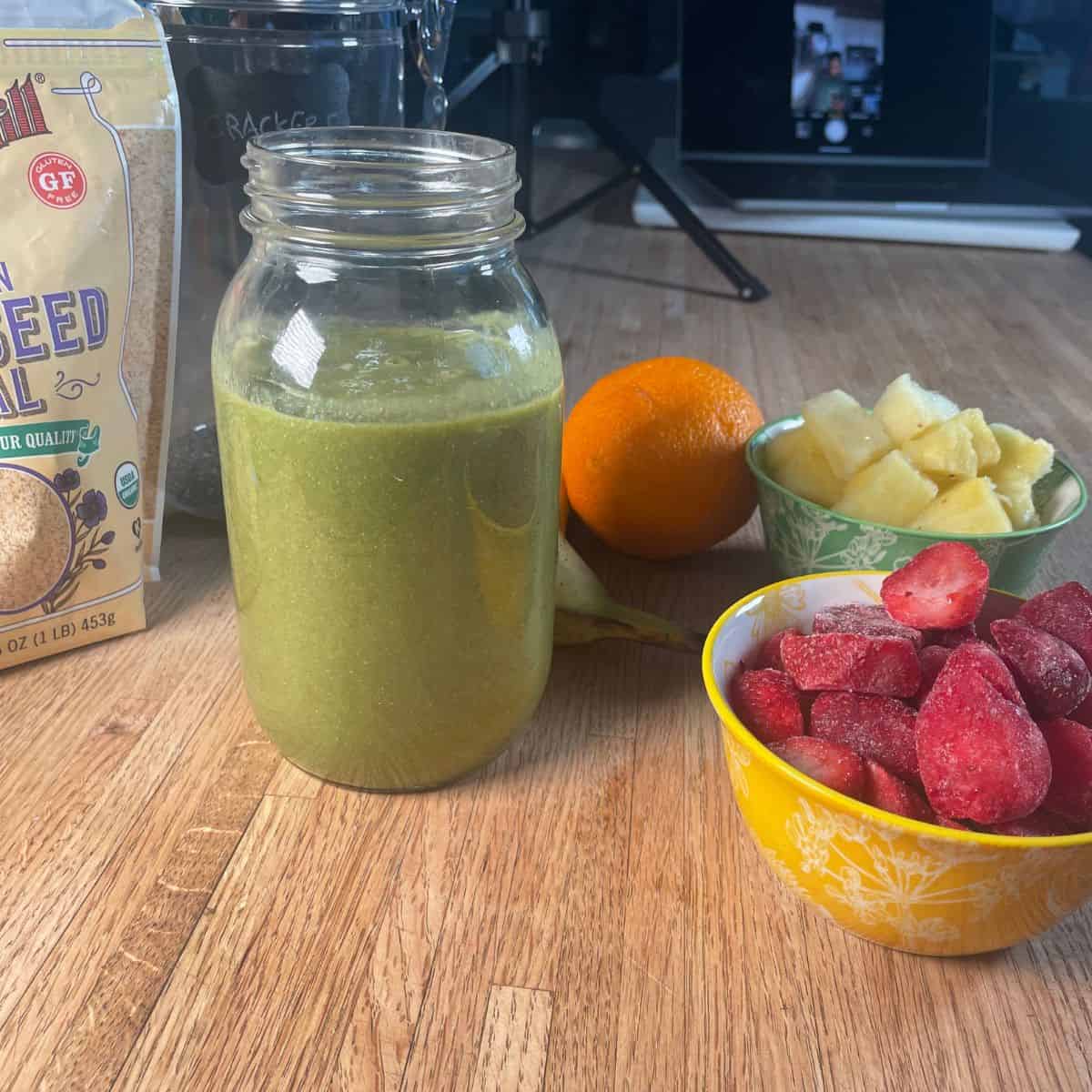 Fresh green smoothie with pineapple, strawberries, and orange on a wooden table.